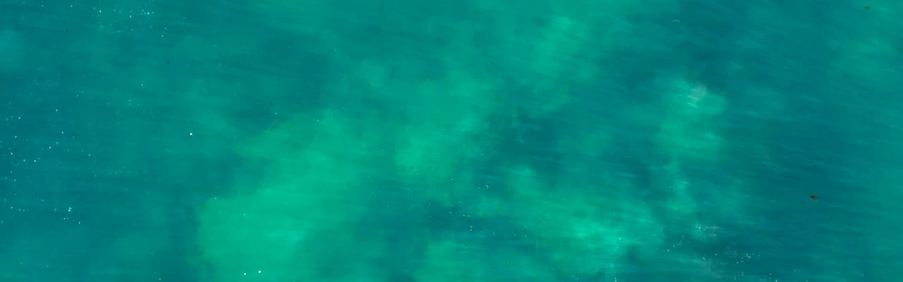 Aerial view of clear turquoise sea water with sunlight patterns over the seabed
